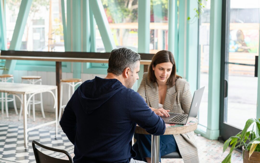 Two people glance at a computer in a cafe