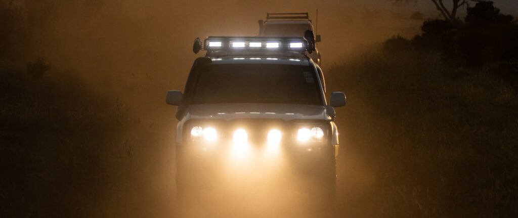 A white SUV drives through a dusty road