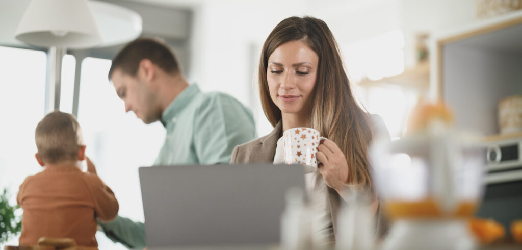 woman looking at a laptop in a kitchen setting with a man and child in the background