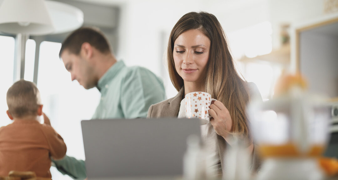 woman looking at a laptop in a kitchen setting with a man and child in the background