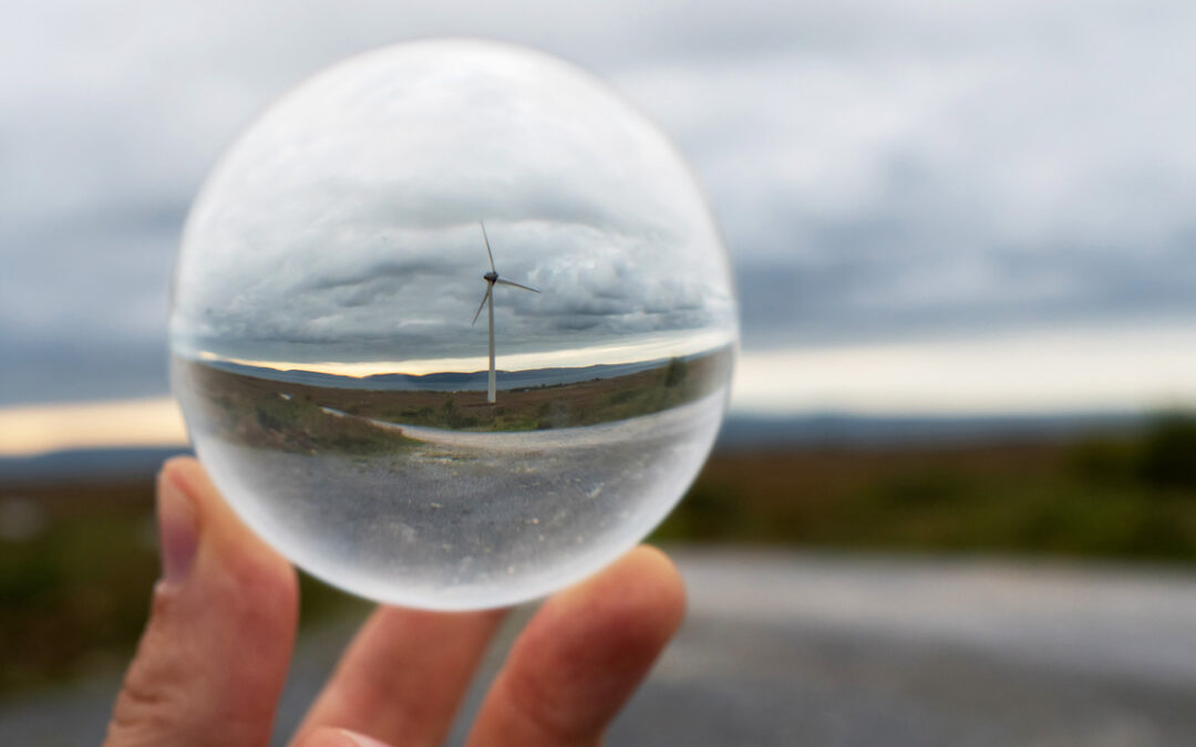 Wind turbine in glass ball in focus. Nature landscape out of focus in the background. Future of wind turbine and green energy production forecast and prediction concept.