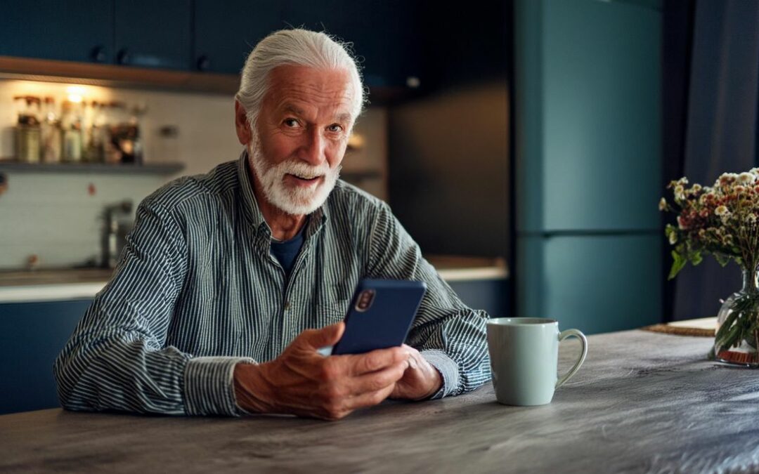 smiling older man using a smartphone at a kitchen table
