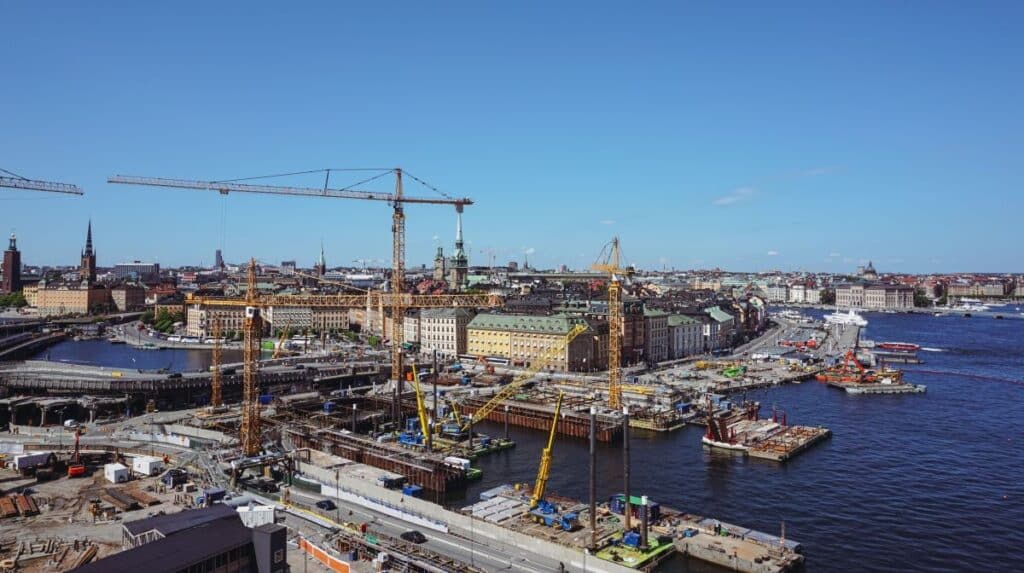 Aerial view of multiple infrastructure construction projects with cranes and waterfront development in a large urban area.