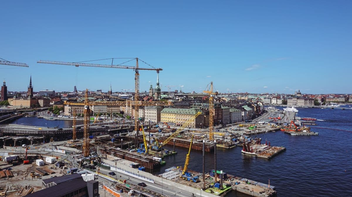 Aerial view of multiple infrastructure construction projects with cranes and waterfront development in a large urban area.