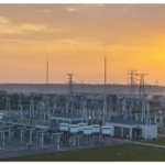 Large-scale thermal power plant under construction with cranes, steel framework, and coastal background