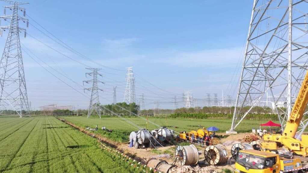 Construction scene with power line towers and workers under high voltage transmission lines in a green field