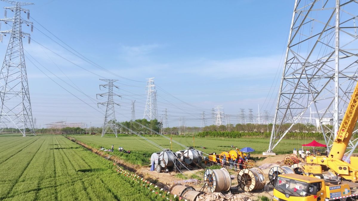 Construction scene with power line towers and workers under high voltage transmission lines in a green field